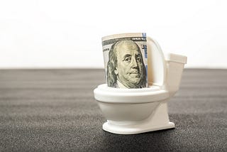 A 50-dollar bill being flushed down a small toilet