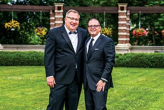 Two men in formal wear pose for a photo on the lawn.