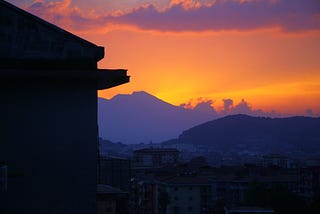 A sunset behind mount Vesuvius, looking over an Italian town with the silhouette of an apartment building in the foreground.