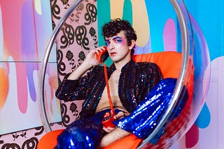 A person wearing colorful makeup and a glittery outfit making a phone call.
