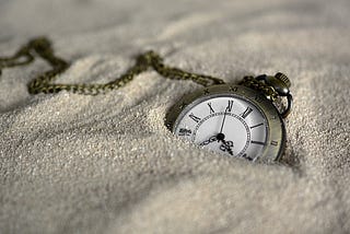 A Pocket Watch With Roman Numerals Lying In The Sand.