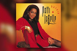 Patti LaBelle’s ‘Burnin’’ album cover: she sits on a chaise lounge with a backing made of thin, curved metal railing. She wears a red skirt suit, with a black top, gold bangles on her right wrist, a gold geometric necklace, and a shiny, gold belt.