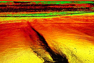 altered photograph of ashes dumped on a beach being washed away. the colors are bright orange, yellow, and green