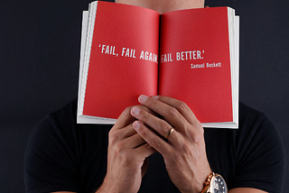 A Man Covering His Face With A Book With The Words, “Fail, Fail Again, Fail Better.” By Samuel Beckett