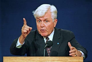 Grey-haired older man waving a finger.