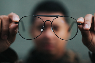 Blurred out person, holding up a pair of glasses in front of them