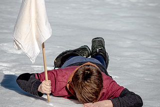 A child face down in the snow with a white flag