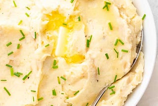 instant pot mashed potatoes served in a white dish, garnished with fresh chives and melted butter