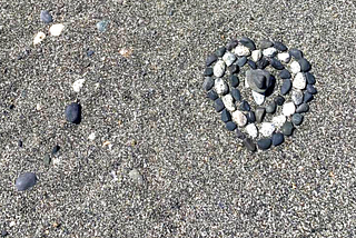 Rocks in the sand in the shape of three hearts, each one formed around the next.