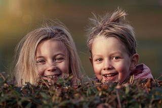 Two small smiling girls with wild hair peeking above a hedge