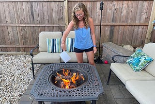 Me in shorts and a tanktop holding a photograph above a fire pit.