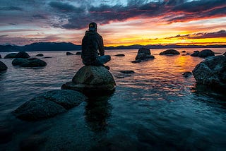 Man on stone by water looking into the distance