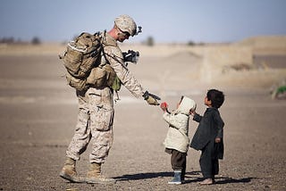 A soldier is giving a red fruit to two small children