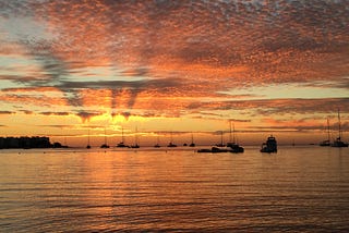 An orange and pink sunset over the ocean just before the sun disappears into the sea.