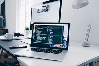 A MacBook with lines of code on its screen on a busy desk.