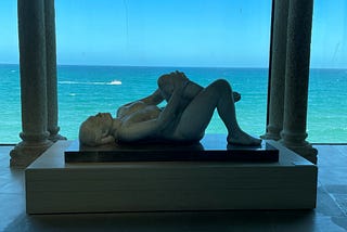 A sculpture of a woman lying down with the sea in the background.