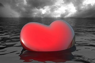 Photo illustration of bright red heart sinking into gray ocean.