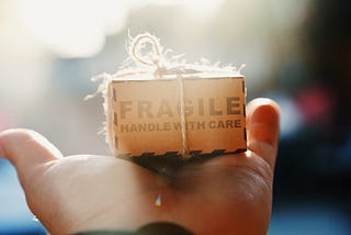 Small packaged box with fragile written on it resting on someone’s open palm