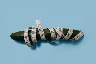 A picture of an english cucumber wrapped in flexible measuring tape.