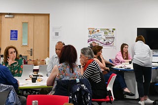 Researchers and facilitators sit in discussion around tables at one of the collaborative lab sessions