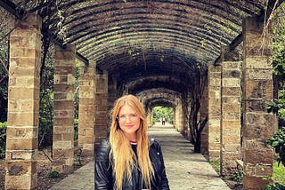 A young blonde in glasses woman standing in the center of a brick archway in Europe