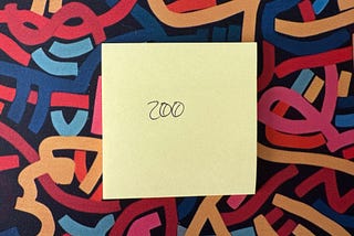 Yellow sticky note with the number ‘200’ written on it in black ink, placed on a colorful abstract background with intertwined shapes in red, blue, pink, and orange.