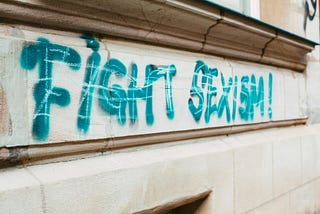 A cement wall with graffiti that reads “fight sexism”
