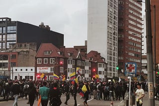 Picture of a protesting crowd, six Colombian flags are being waved by protesters.
