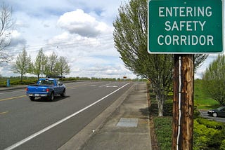 A truck drives past a green road sign that reads, “ENTERING SAFETY CORRIDOR”