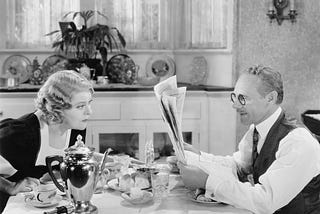 A man and woman sitting at a table reading a newspaper