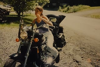 Photo of a thin young woman sitting on a large motorcycle.