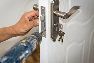 Hand with drill replacing lock on a white door