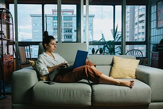 Woman working on laptop while lounging on couch at home