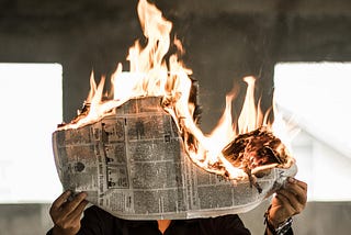 A man holds a newspaper on fire as a metaphor for the demise of news media.
