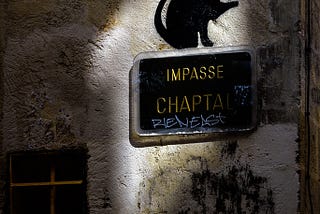 textured wall with a small window and graffiti. On the wall is a sign that reads impasse chapta and a spray painted black cat