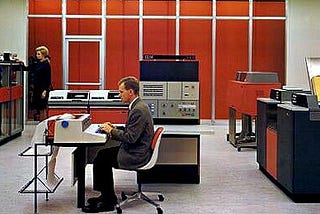 Two people are operating large computers and mainframes. Image from the IBM archives.