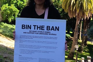 Image of Awatea at the launch of the Open Letter holding a sign that reads ‘Bin the Ban’ with Myers Park and the city in the background.
