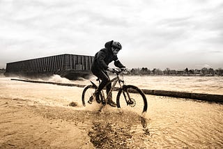A man pedals a bike through ankle-deep water.