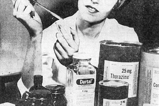 Black and white picture of a nurse from the 1960s filling up a medication dose from a bottle using a dropper. Several psychotropic medications are in front of her including Thorazine and Dartal.