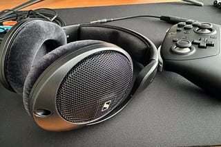 A pair of Sennheiser HD560S headphones lying on their side on a desk mat near a Switch 2 Pro controller.