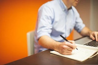 a man is writing on a notebook_write my essay