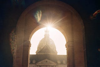 An image of L’Hôtel des Invalides in Paris, with a solar flare peeking through an archway