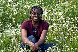 African American woman in a maroon v-neck t-shirt and jeans sitting in a field of flowers