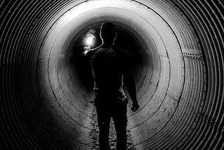 Man in a dark tunnel with no light at the end.