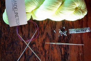 Neon yellow yarn, circular knitting needles, crochet hook, and beads