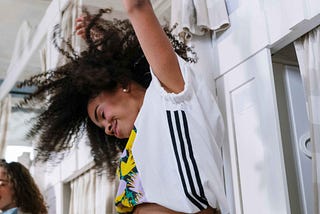 Woman dancing with arms up, head tilted to side and forward with eyes closed and smiling.