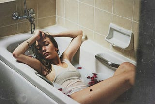 Woman in bathtub with soapy water and rose petals