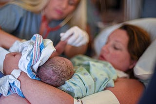 Woman holding newborn baby with midwife by her side.