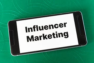 A phone sits on a green background with words written “influencer marketing”.