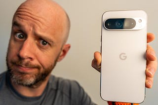 Mark Ellis holds up a white Pixel 9 Pro XL to camera. He looks intrigued.